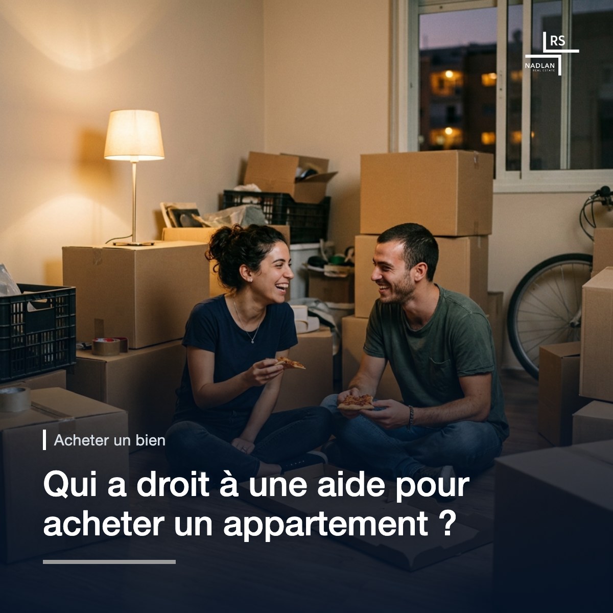 Un jeune couple assis par terre dans son premier appartement, au milieu des cartons de déménagement, mangeant une pizza à même la boîte