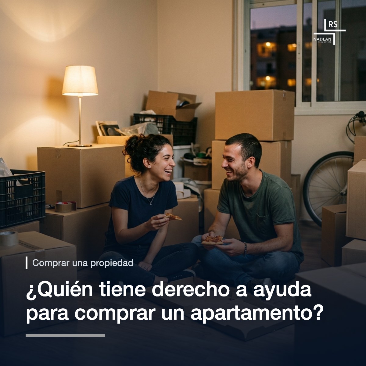 Una pareja joven sentada en el suelo de su primer apartamento entre cajas de mudanza, comiendo pizza directamente de la caja